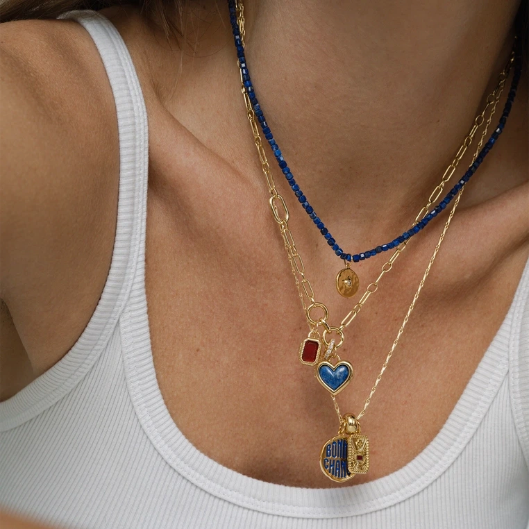 Close-up of a person wearing multiple gold necklaces with various pendants on a white background