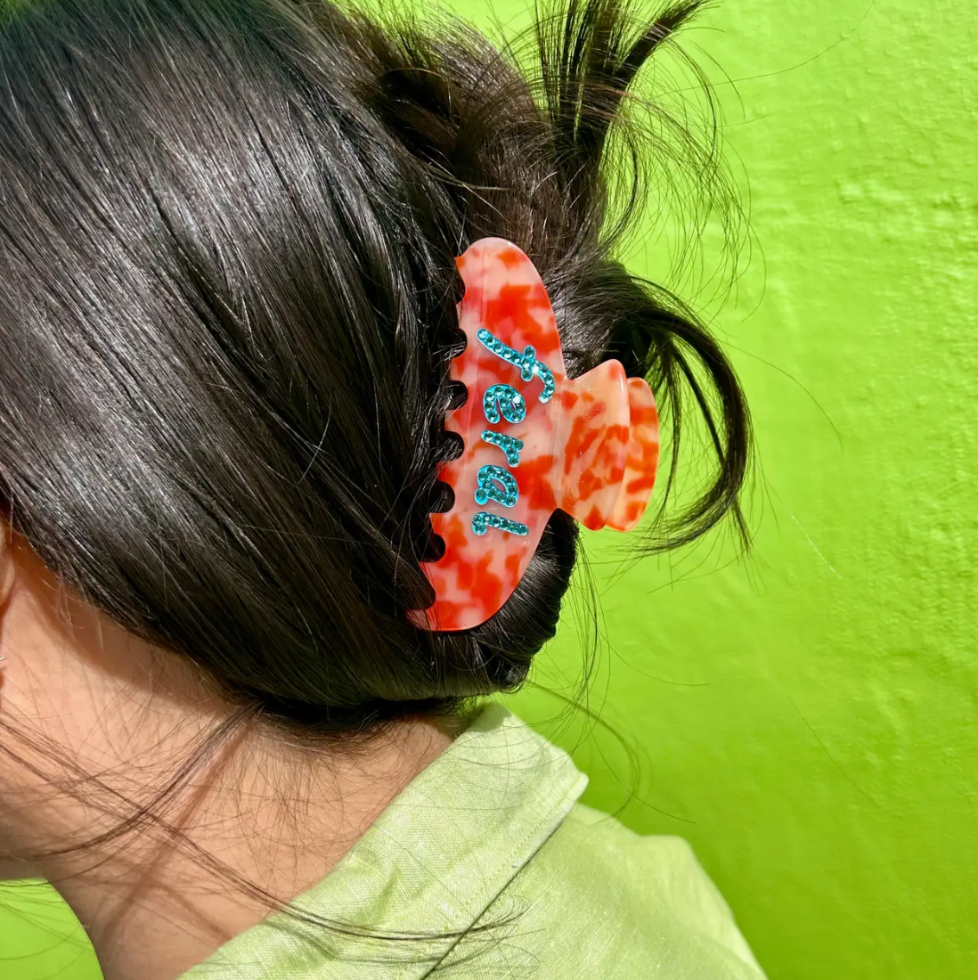 vibrant red and orange tortoise hair claw with bright blue rhinestones spelling "Feral" Design is on both sides and is beveled with blue fill and rhinestone overlay.