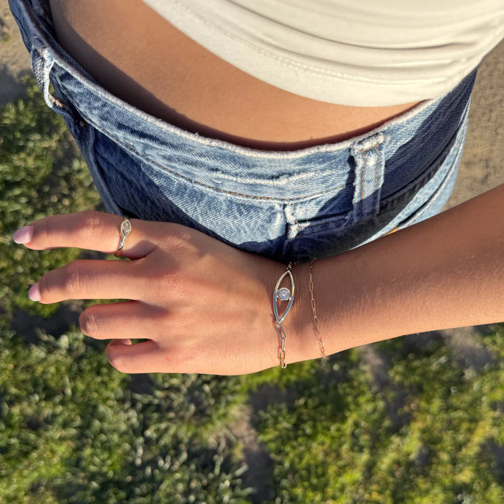 Hand wearing a ring and bracelet with denim shorts in the background