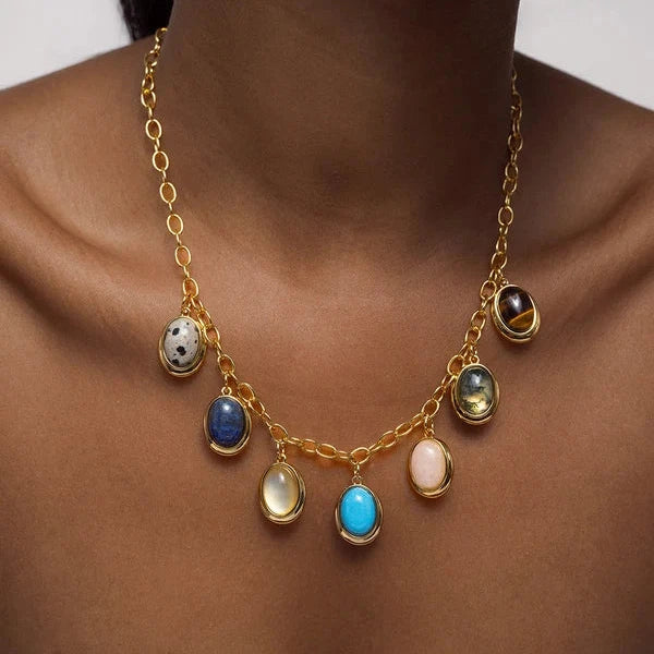 A gold chain necklace with seven dangling oval gemstone charms in various colors, worn on a model's neck.