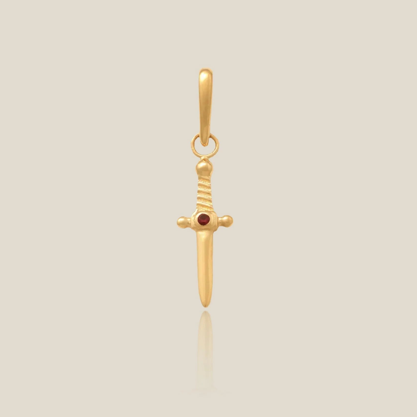 a gold dagger shaped charm with a red stone over a beige background