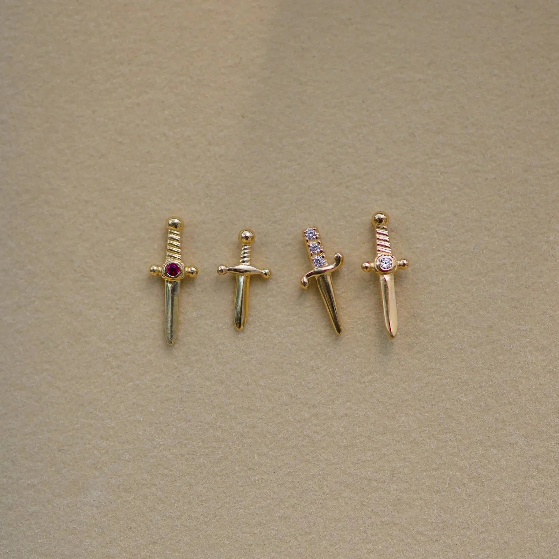 Four gold sword-shaped charms with gemstones on a beige background