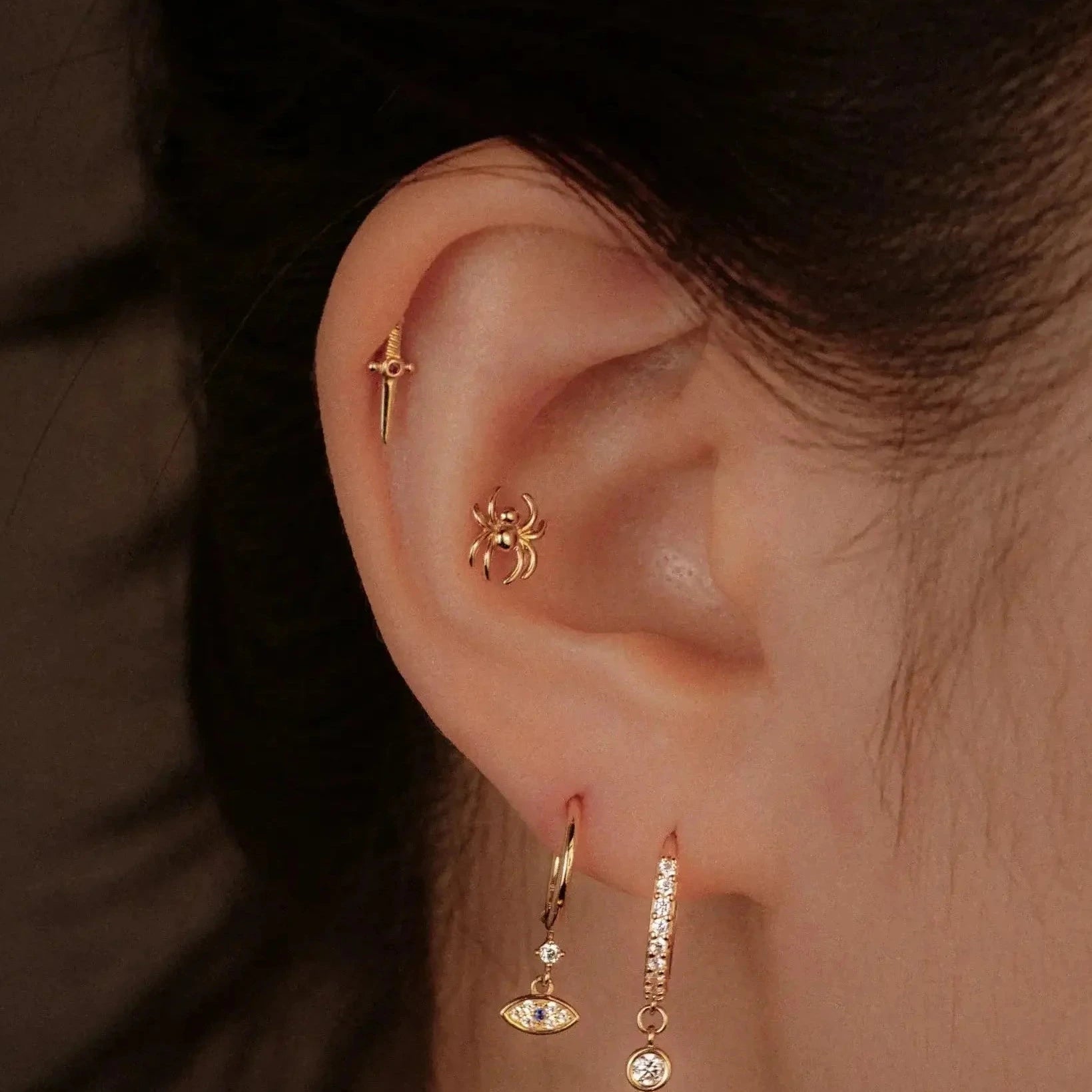 Close-up of an ear with gold earrings against a brown background