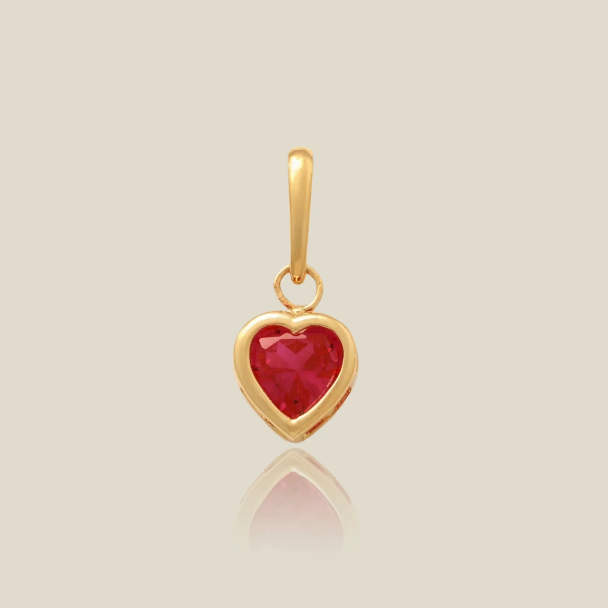 a gold heart shaped charm with a red stone over a beige background
