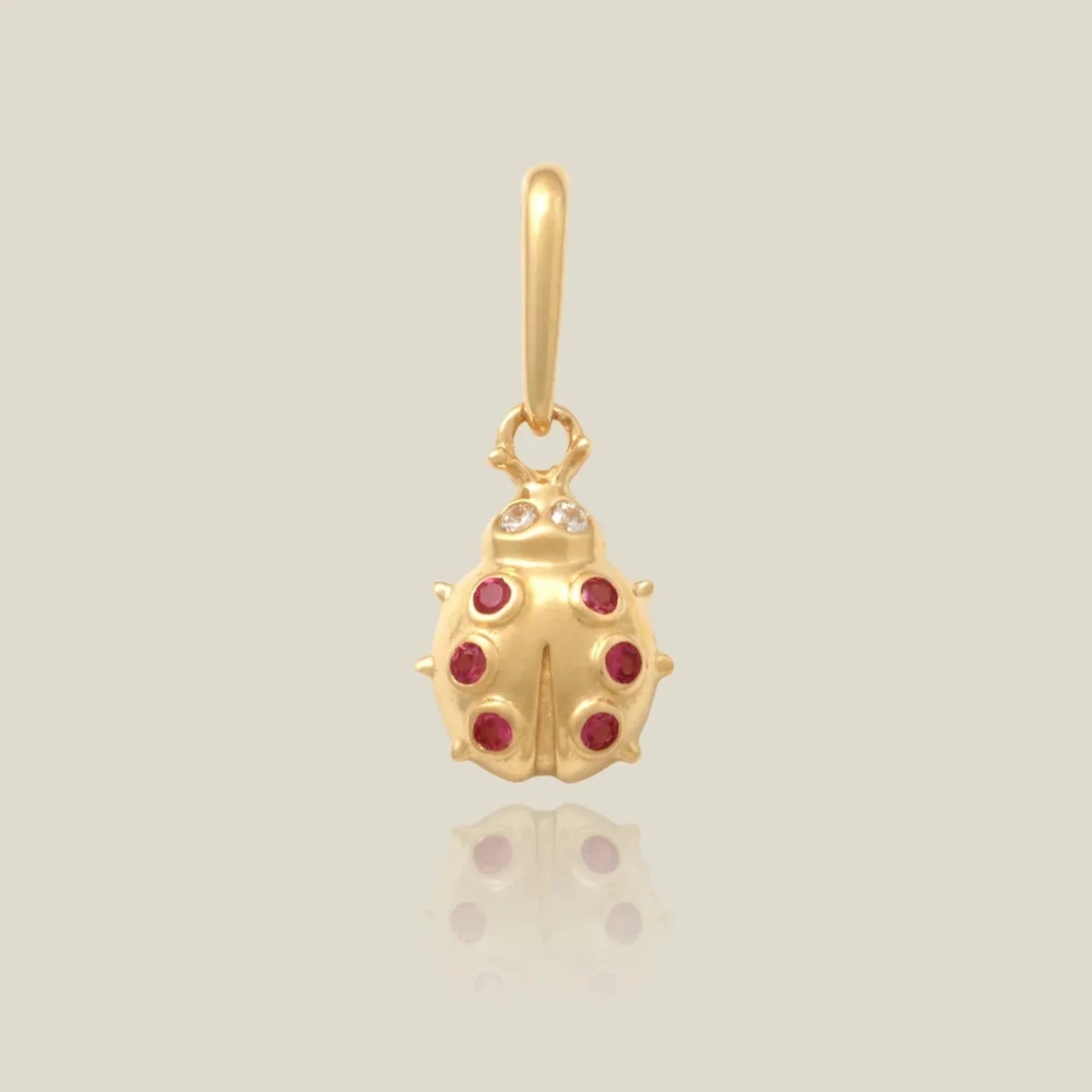 a gold charm shaped like a ladybug with red stone accents over a beige background