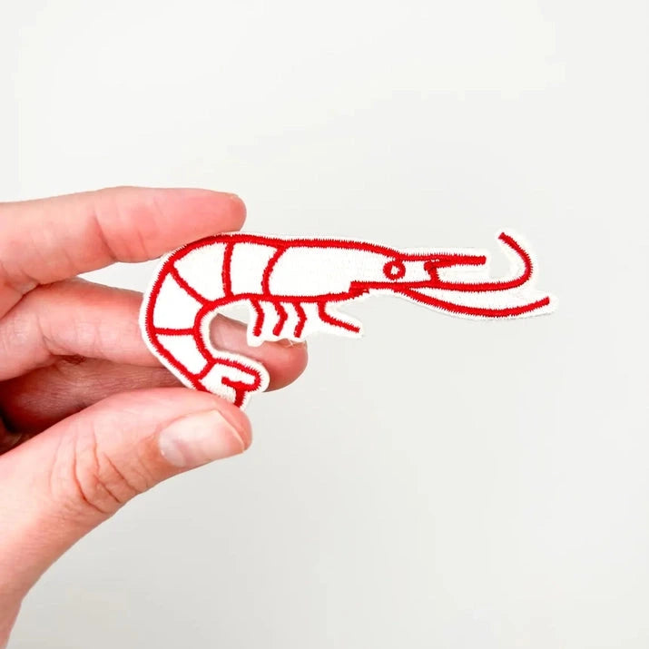 a red and white iron on patch of a shrimp held by a hand over a white background