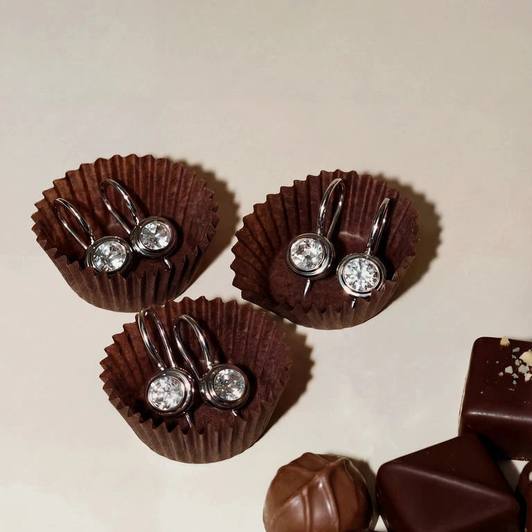 silver earrings with bezel set white sapphires in chocolate wrappers on a neutral background