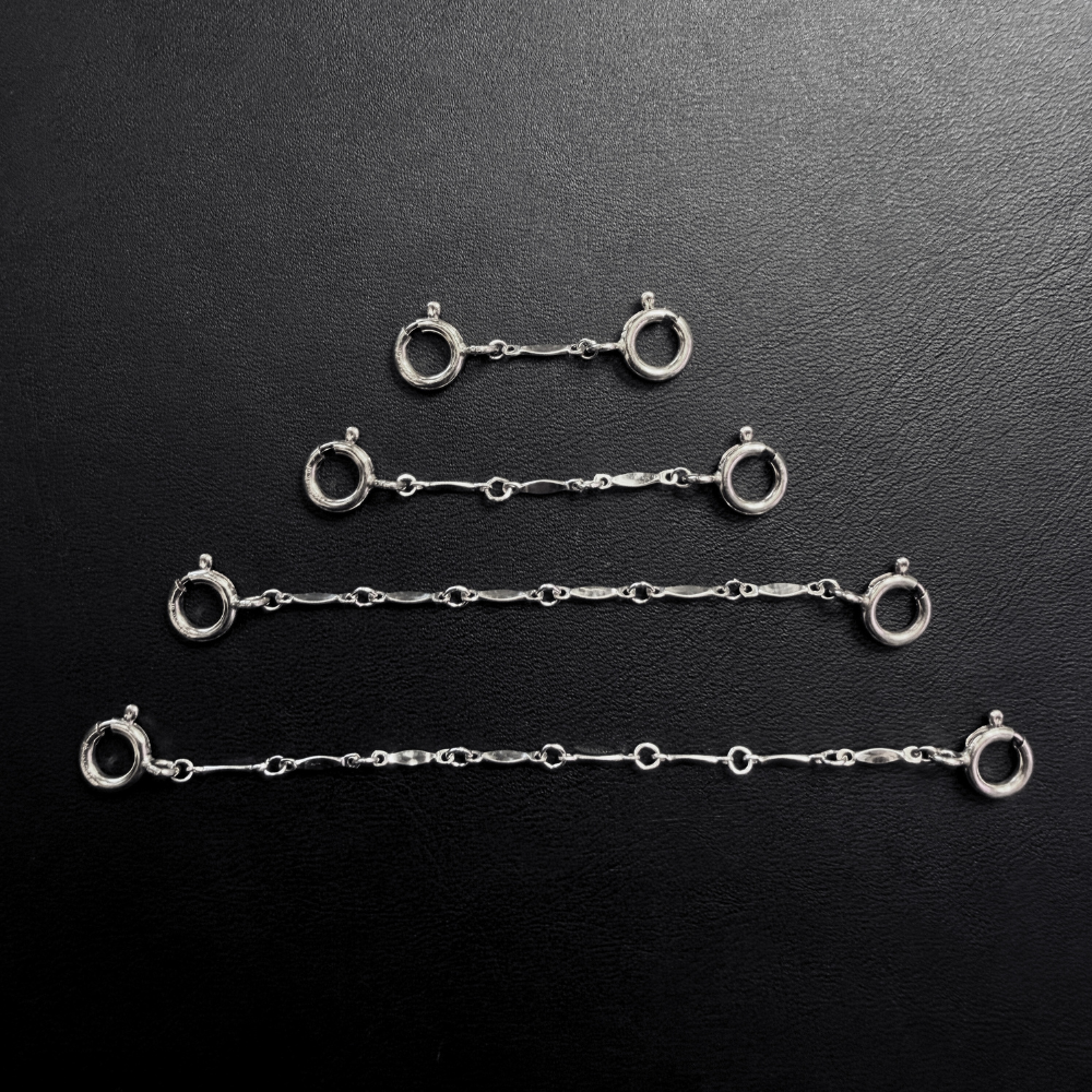 four sterling silver bar chain extender chains attached to jumbo clasps on a black leather background