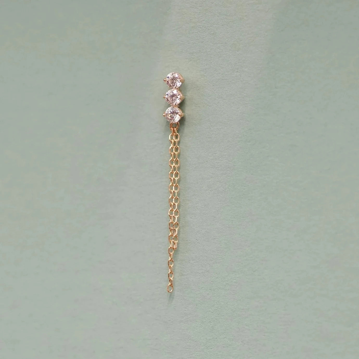Gold chain earring with pink gemstones on a light green background