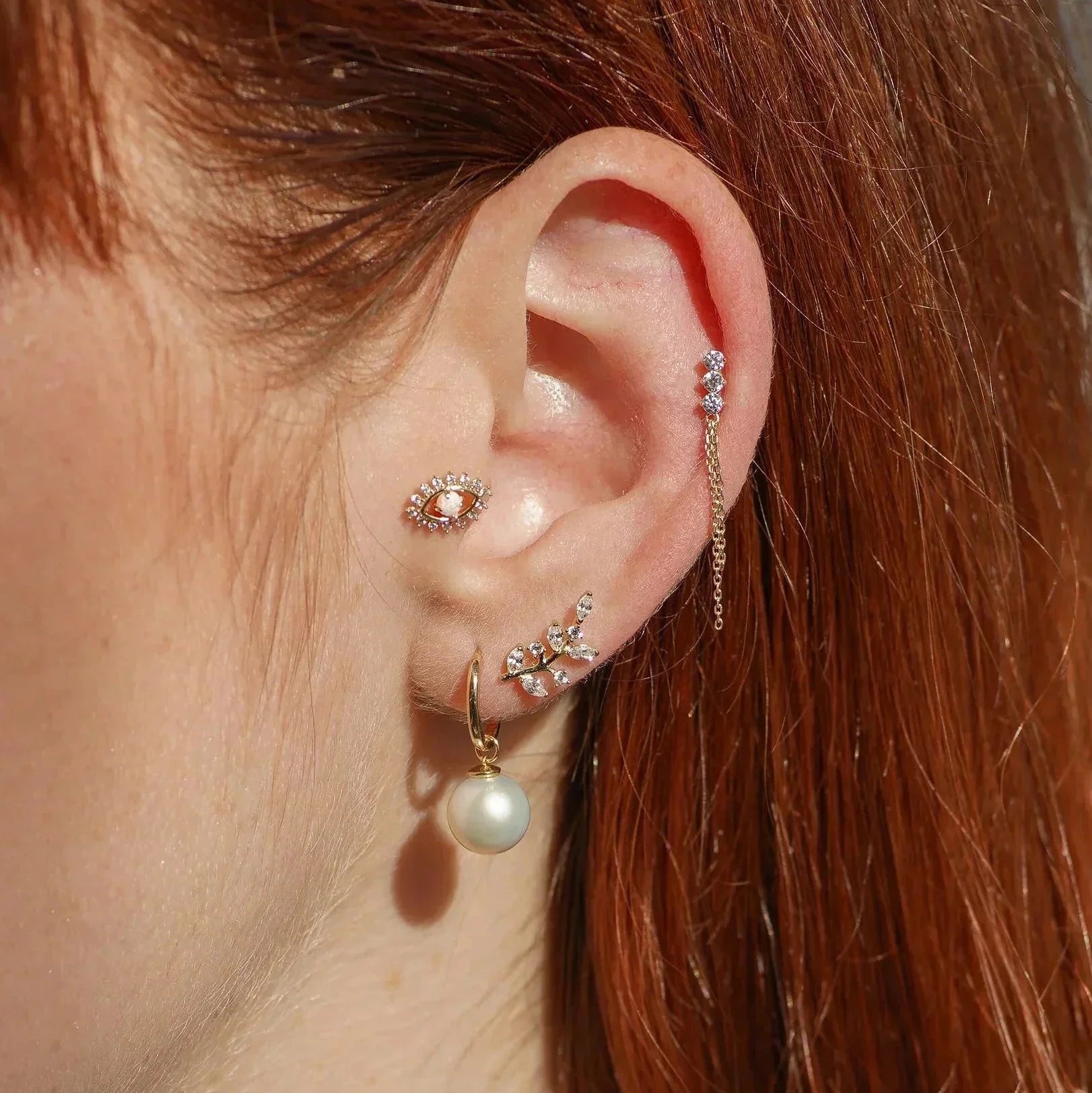 Close-up of an ear with multiple earrings on a person with red hair.