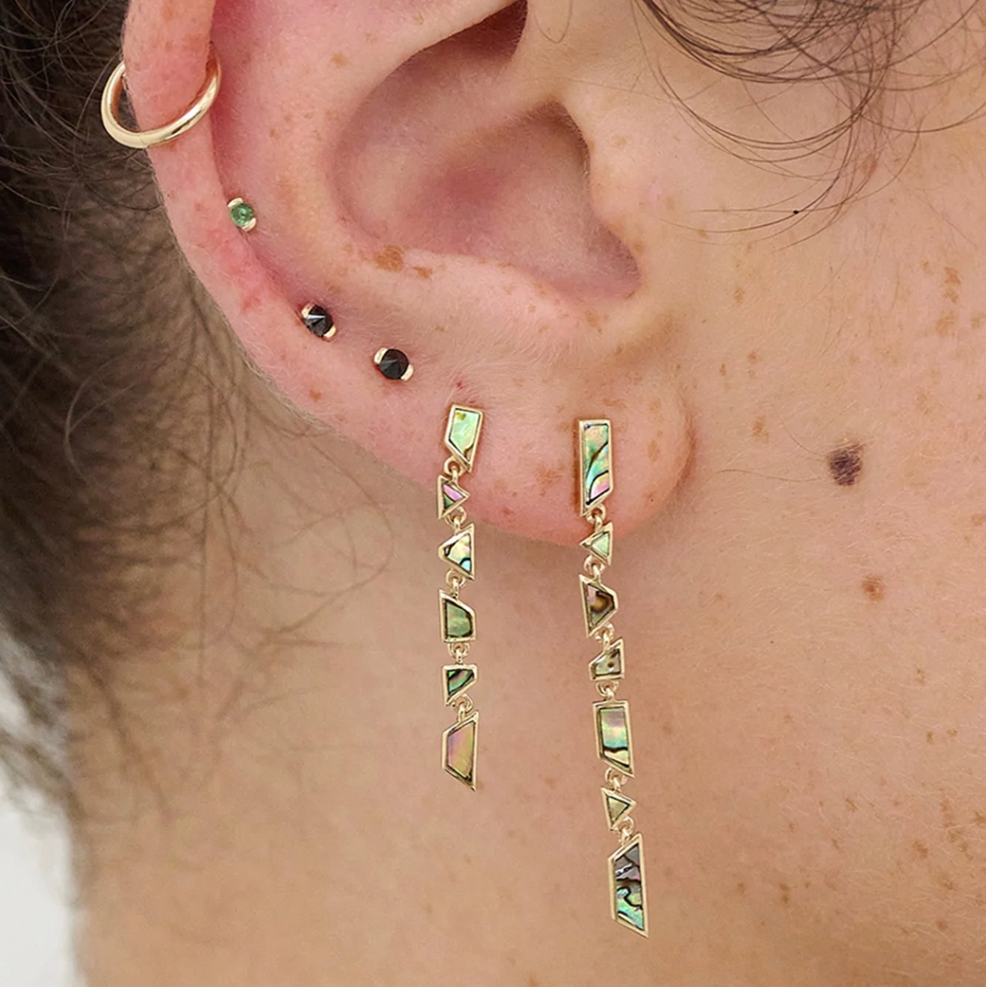 Close-up of an ear with gold and abalone geometric  earrings.
