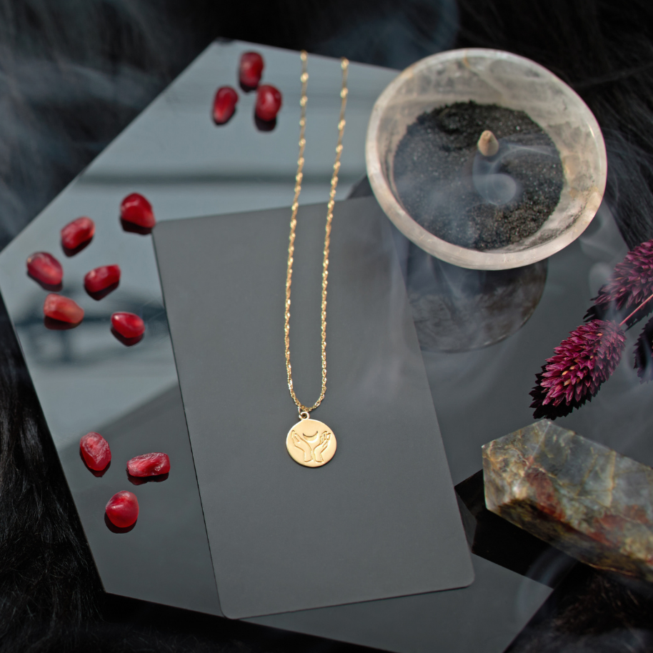 Gold necklace with a pendant on a dark surface with red stones and a small bowl.