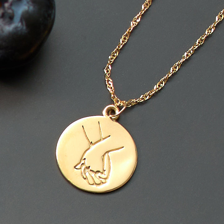 Gold necklace with a round pendant featuring an engraved design on a dark surface.