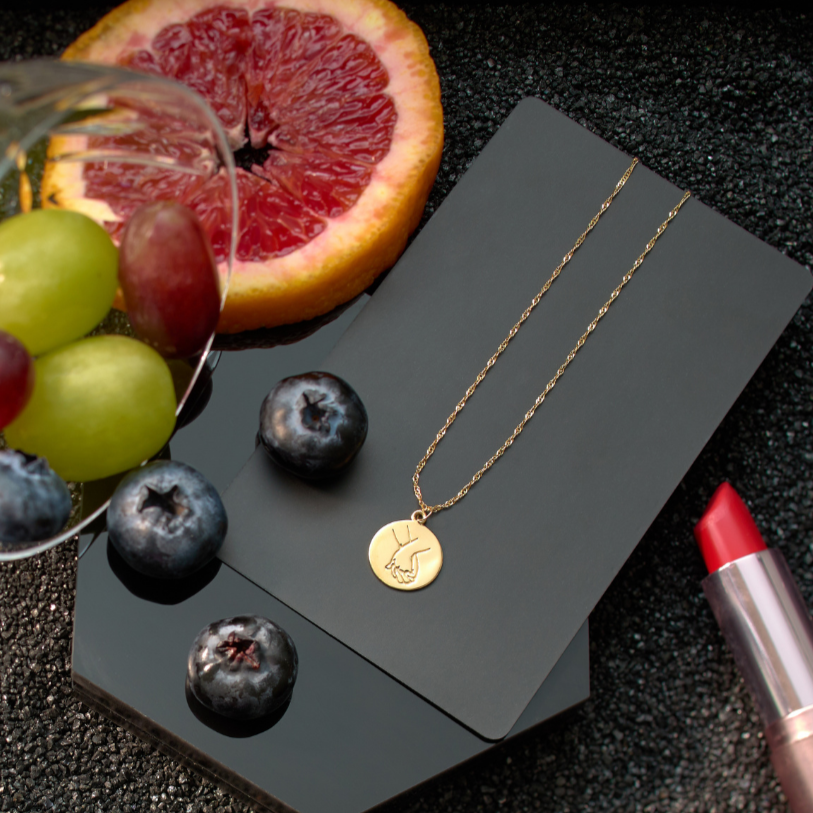 Gold necklace on a black card with grapes, blueberries, and a cut grapefruit on a dark surface.