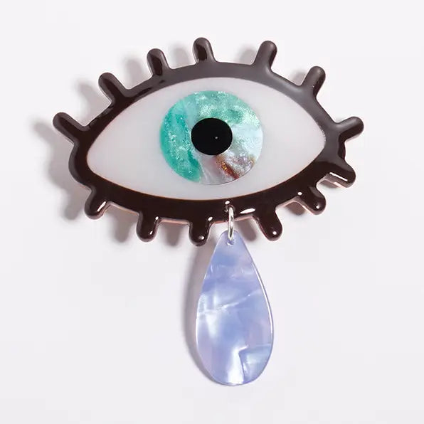 Barrette style hair clip shaped like an eye with a teardrop pendant on a white background
