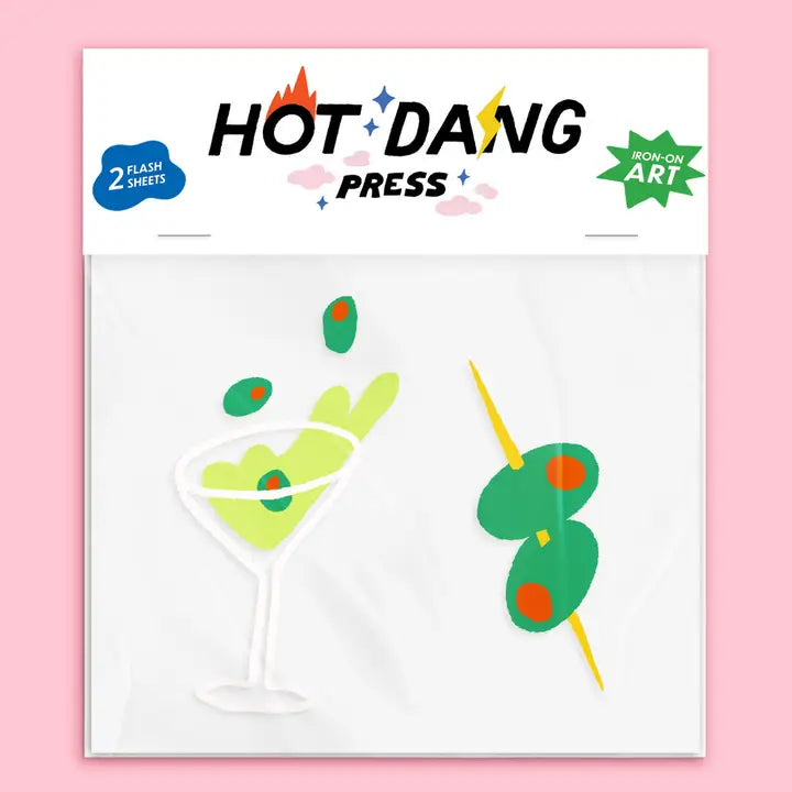 Packaged Hot Dang Press novelty art sheets featuring a martini glass with green olives and a cocktail pick with green olives, on a pink background.