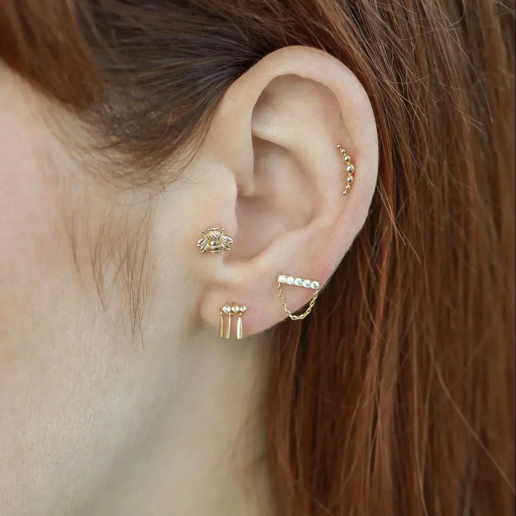 Close-up of an ear with gold earrings and a small hoop earring.