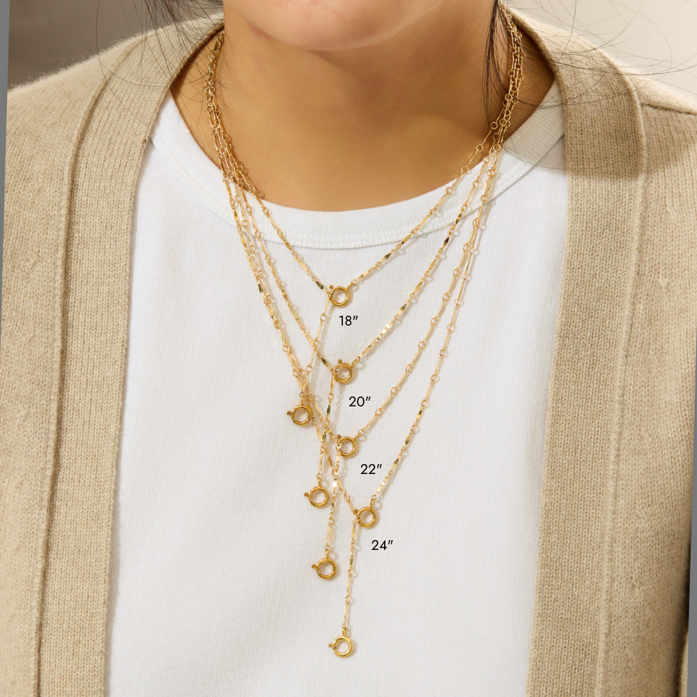 Gold necklaces layered on a person wearing a beige cardigan and white shirt.