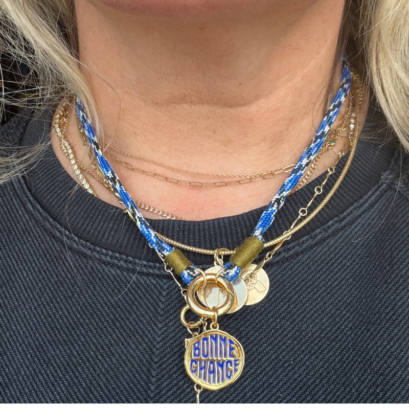 Necklace with blue and gold accents and a 'Bonne Chance' charm on a person wearing a dark shirt.
