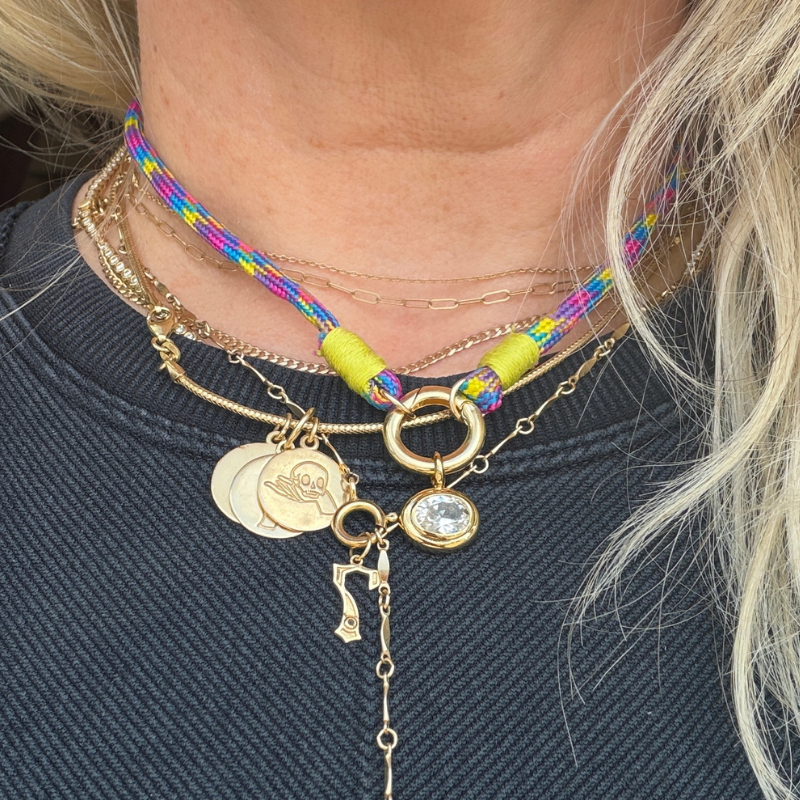 Close-up of a person wearing multiple necklaces with various charms on a dark background