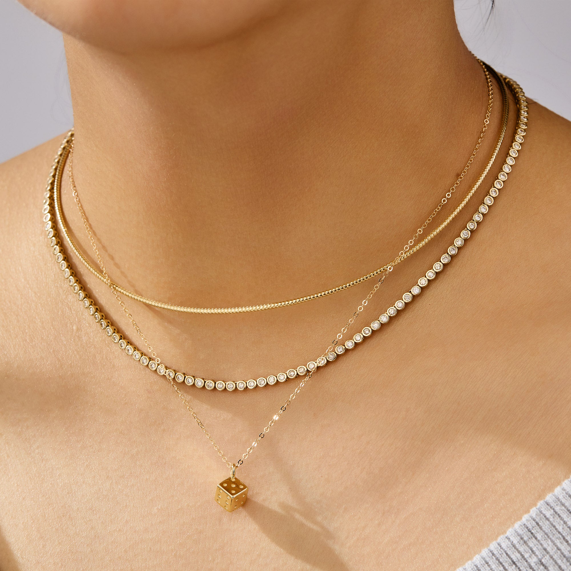 Close-up of a person wearing two gold necklaces with a small pendant on a neutral background