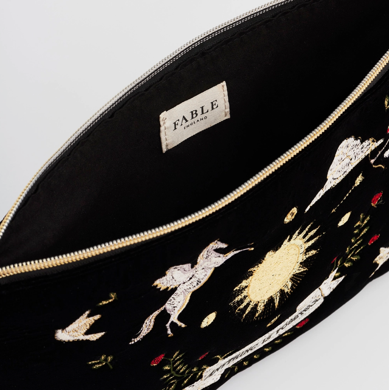 Black pouch with gold zipper and embroidered designs on a light gray background