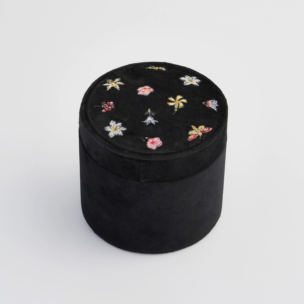Black cylindrical jewelry box with floral embroidery on a white background