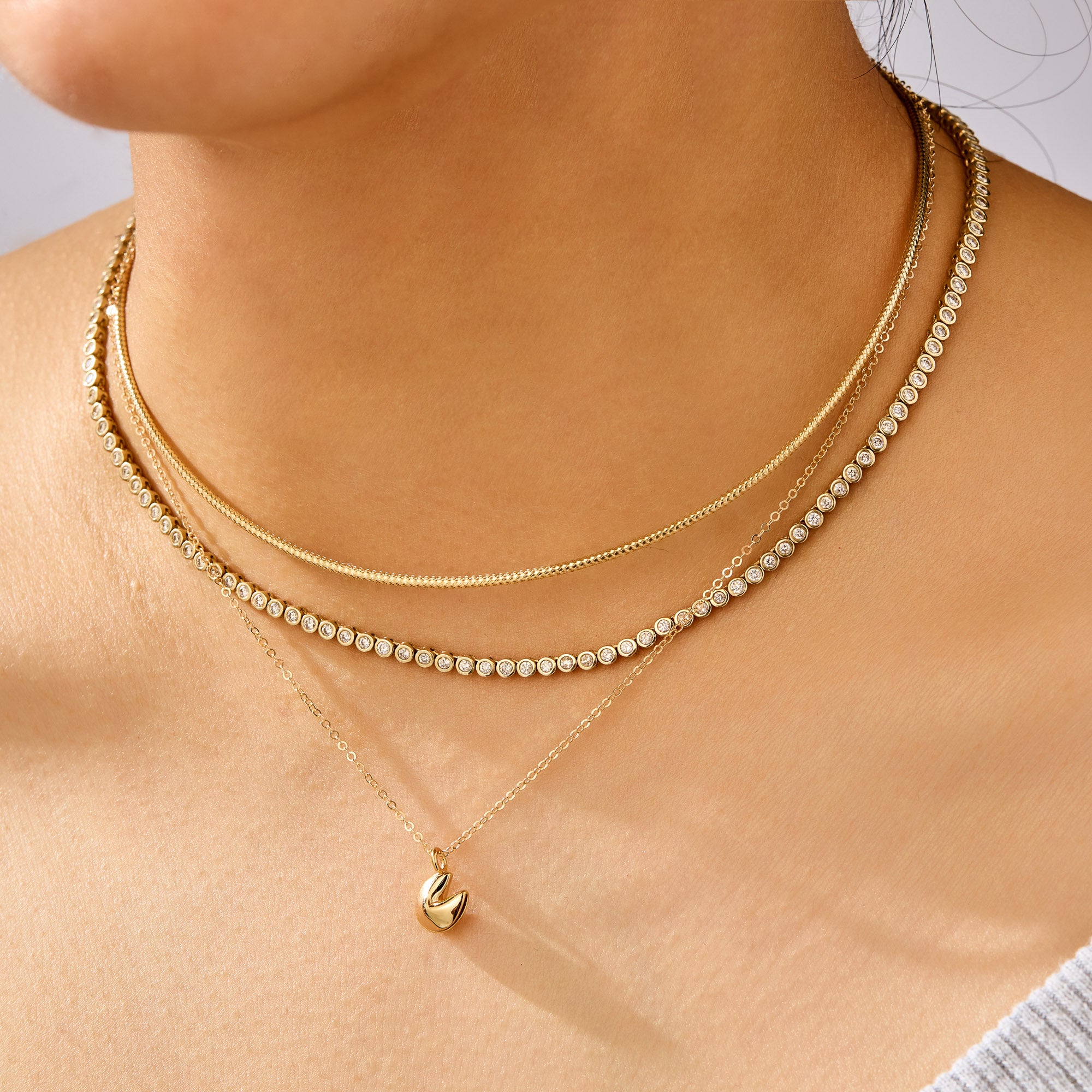 Close-up of a person wearing multiple gold necklaces with a plain background