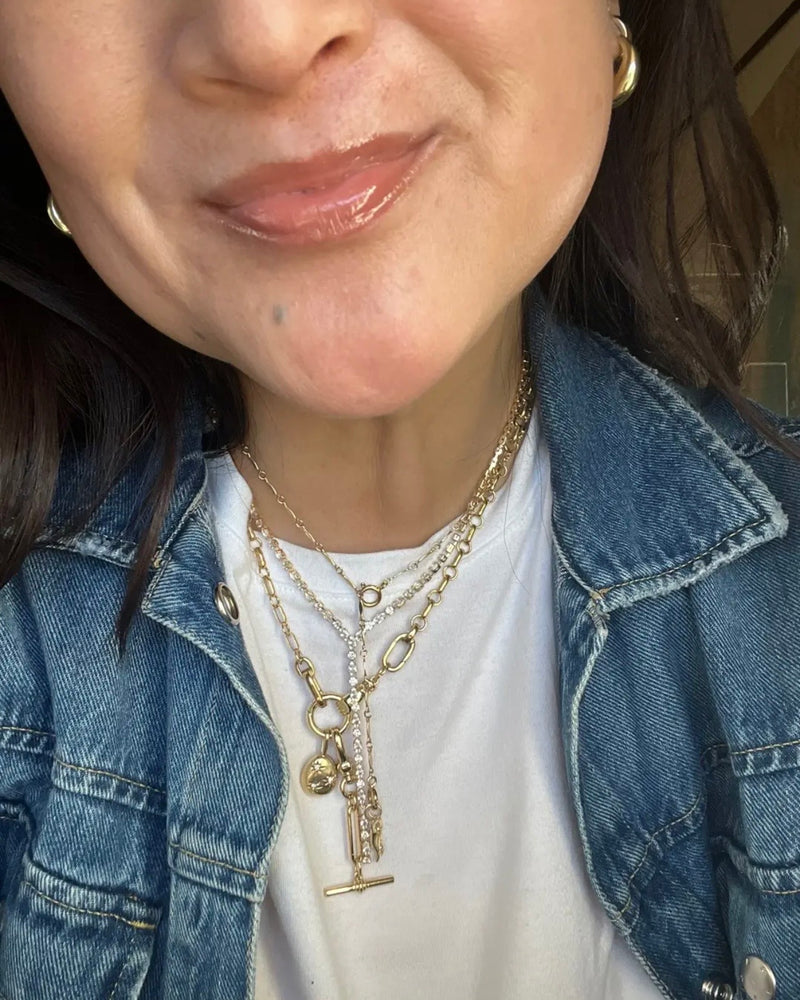 Close-up of a person wearing multiple gold lariat necklaces and a denim jacket.