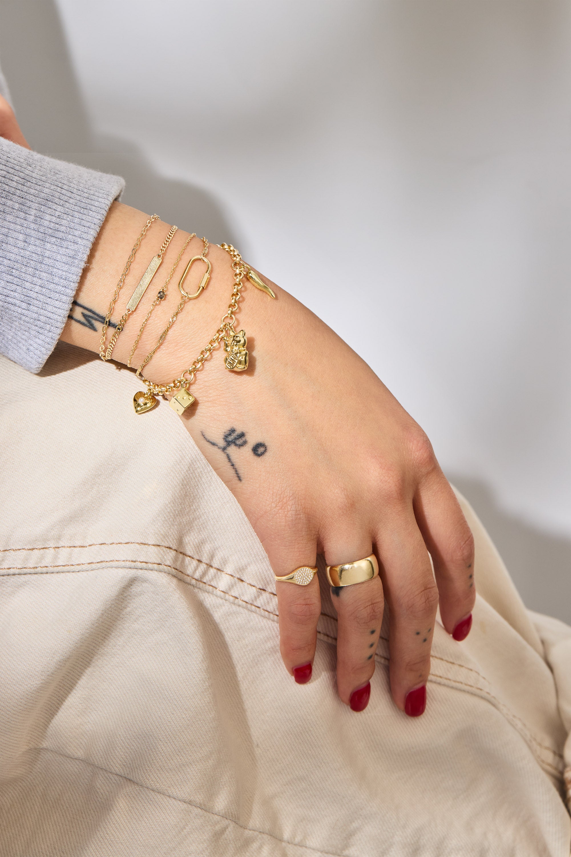 Hand with gold charm bracelet jewelry and tattoos on a neutral background