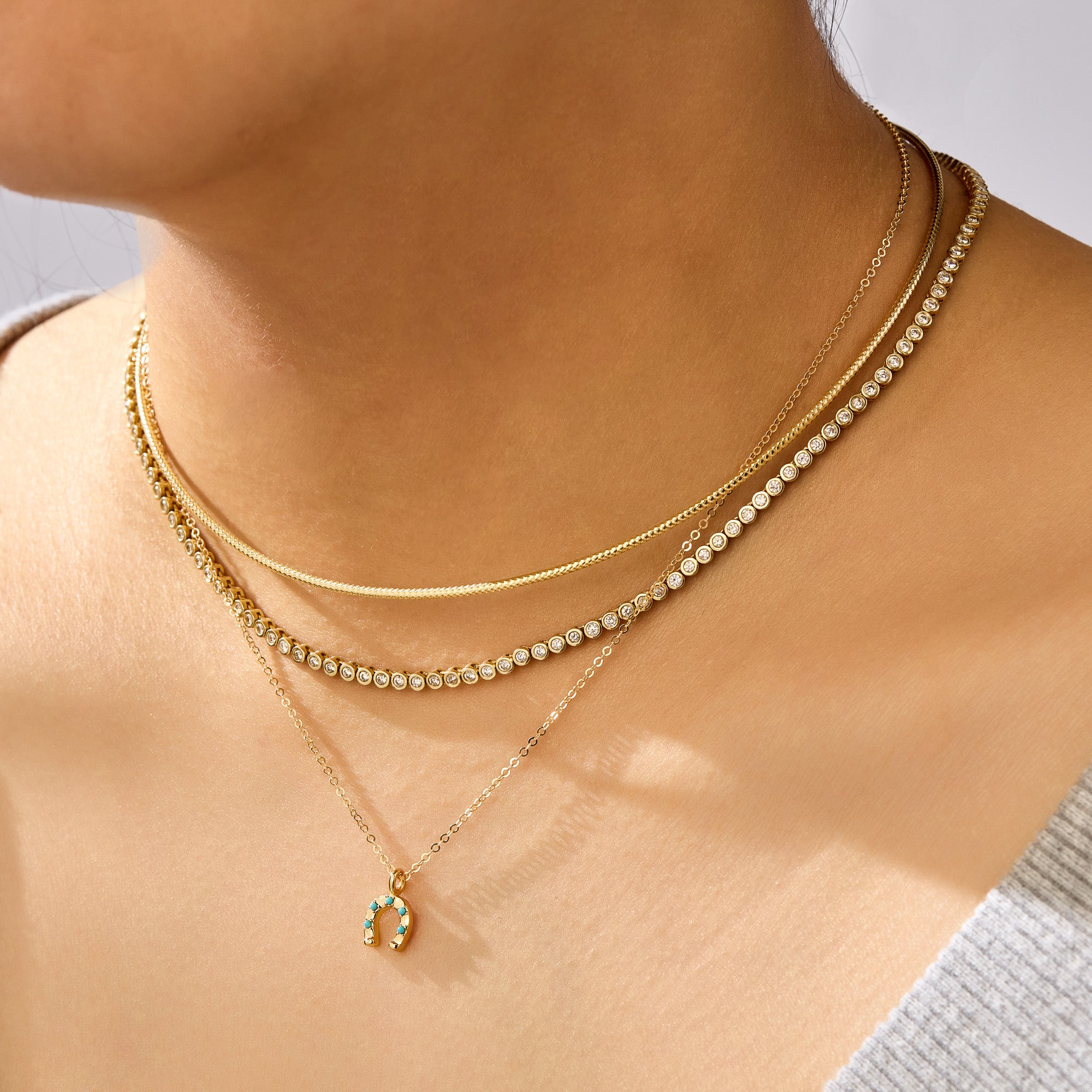 Close-up of a person wearing two gold necklaces with a small pendant on a neutral background
