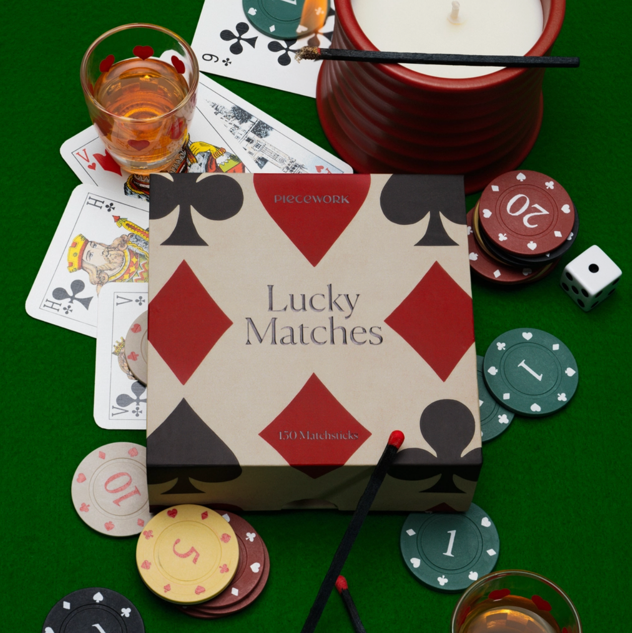 Matches box labeled 'Lucky Matches' surrounded by playing cards, poker chips, and a candle on a green surface.