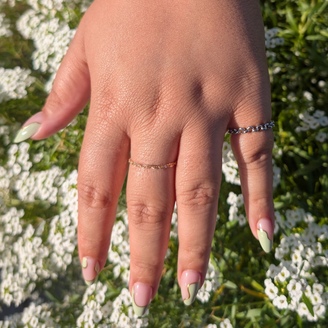 Hand with multiple bracelets and rings against a white flower background