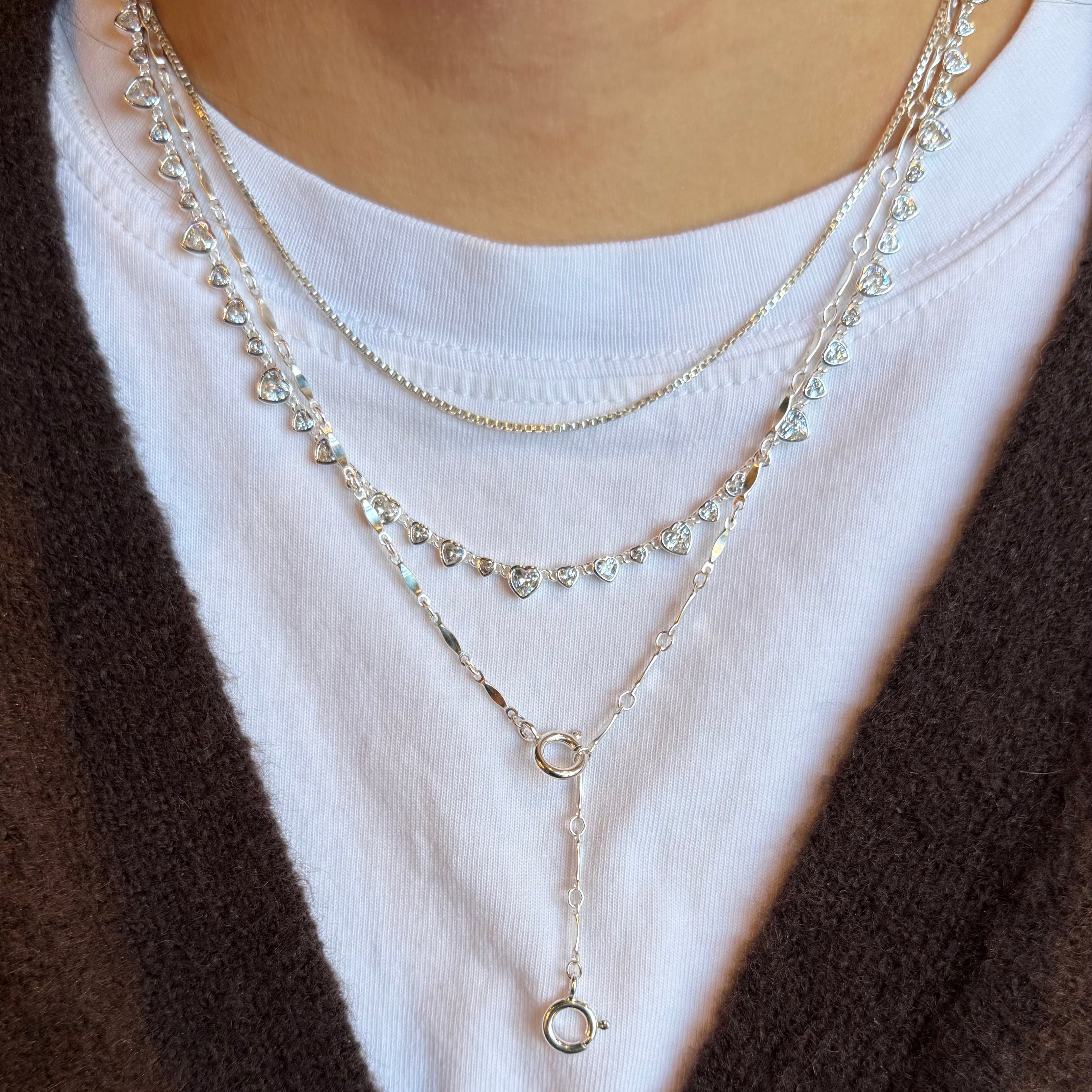 Layered silver necklaces on a white shirt with a brown sweater